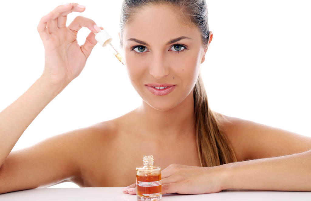 Portrait of a beautiful woman who is applying cosmetic oil over a white background